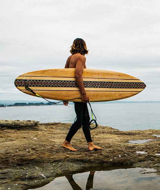 Guy on a beach with an UGGxGrain surfboard
